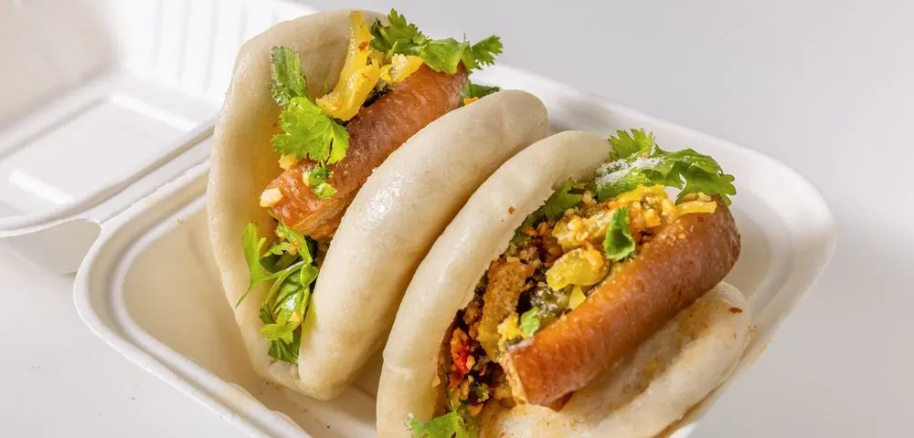 Two steamed buns filled with braised pork belly, pickled cabbage, cilantro, and peanuts